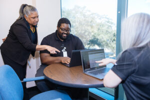 Employees in a discussion while looking at information on their laptops.