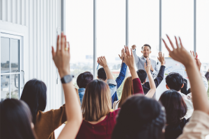 Man pointing at a group of people with their hands raised to ask a question.