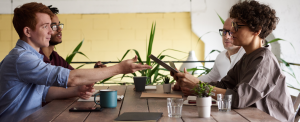 Four employees having a discussion at a restaurant dining table passing around a tablet device.
